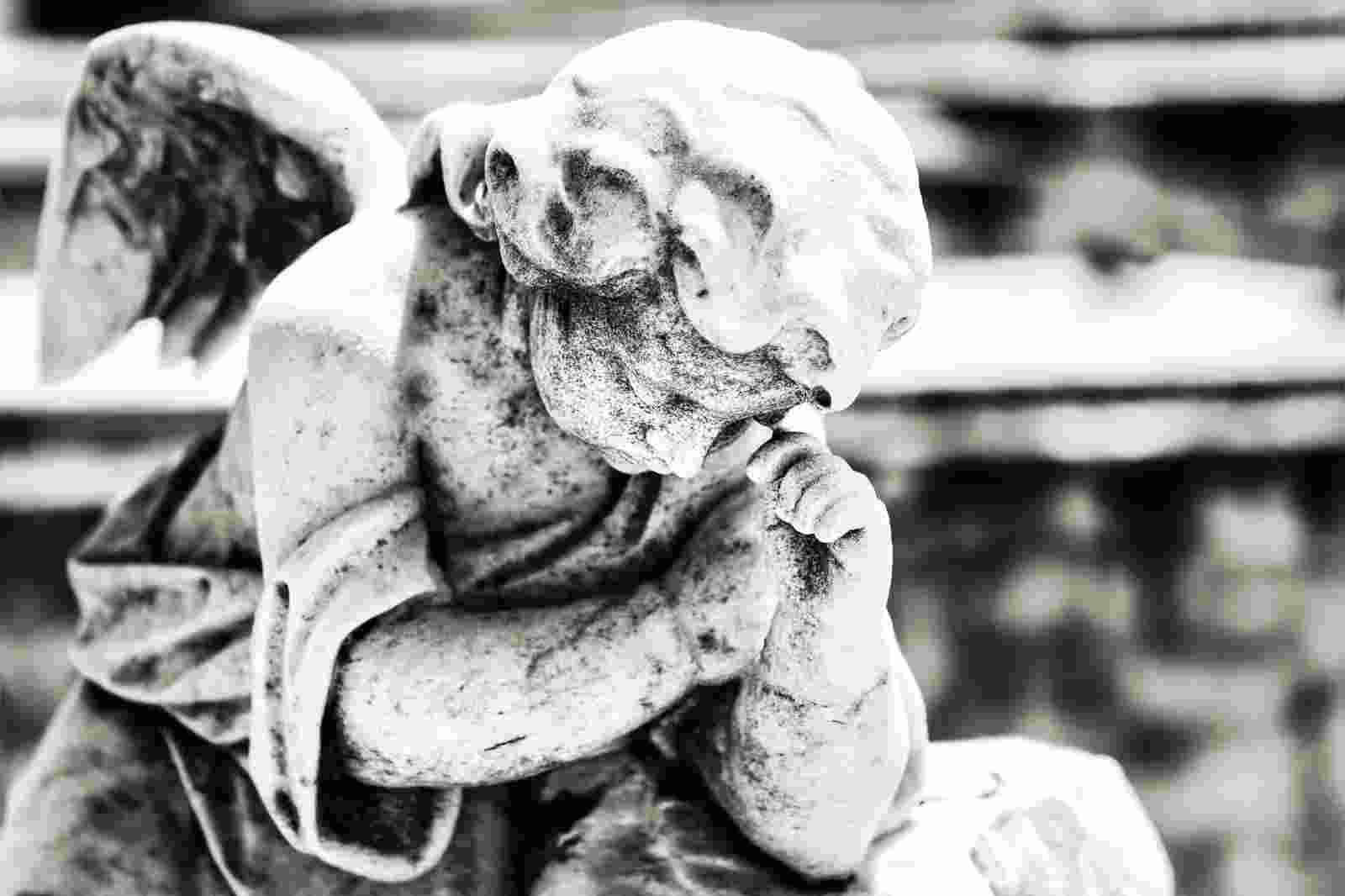 Black and white vintage image of a sad mourning angel on a cemetery with a diffused background